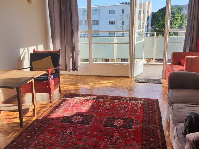 Bright living room featuring classic parquet flooring and direct access to a private balcony through large glass doors.