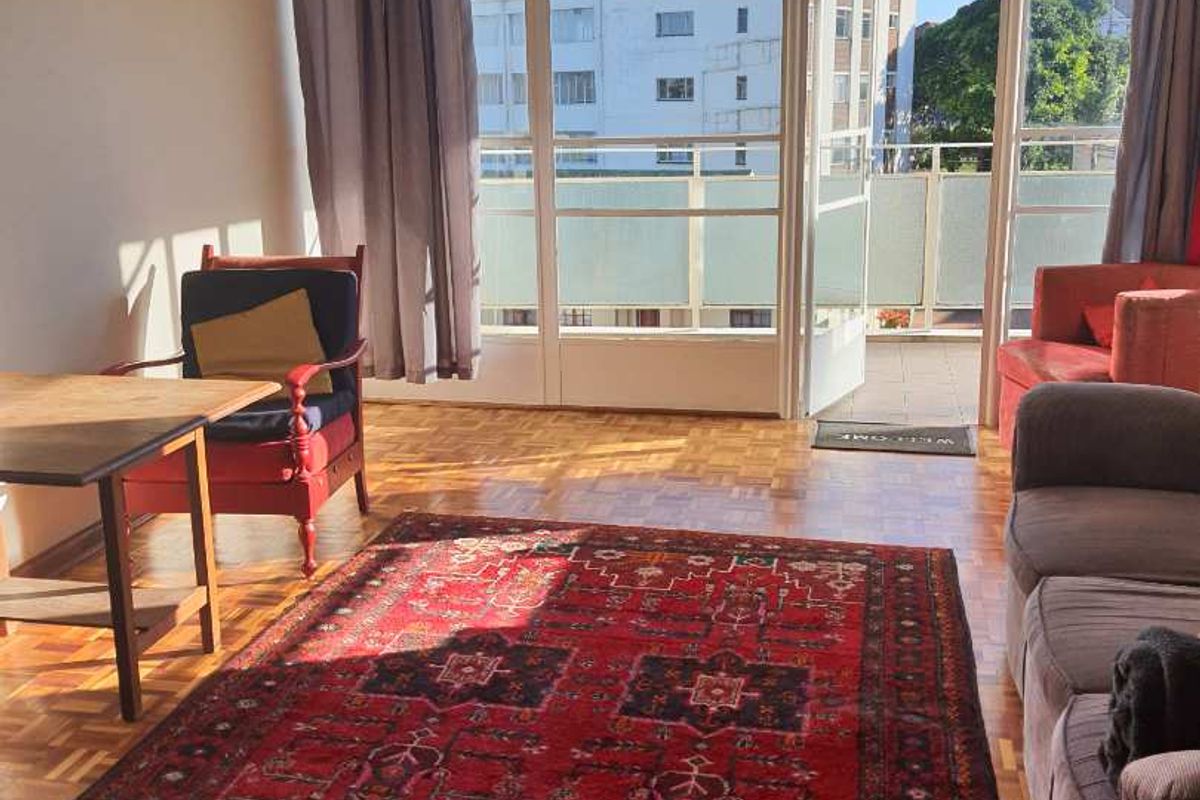 Bright living room featuring classic parquet flooring and direct access to a private balcony through large glass doors.