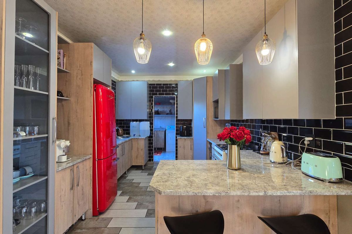 Modern kitchen featuring wood-grain cabinetry, stone countertops, black subway tile backsplash, and a central island with pendant lighting.