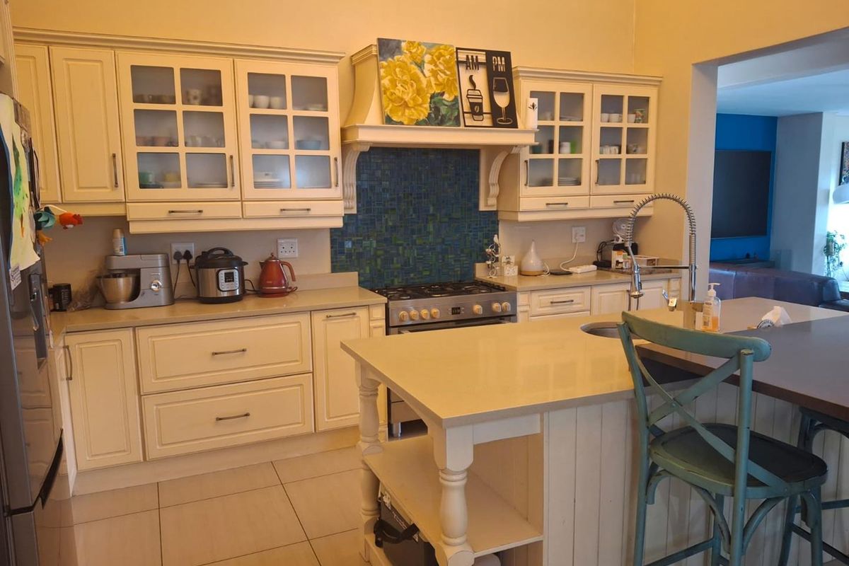 A well-appointed kitchen featuring cream cabinetry, a central island with a prep sink, a mosaic tile backsplash, and a stainless steel gas range.