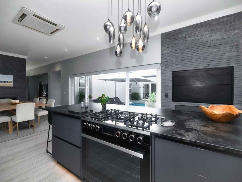 Modern open-plan kitchen and dining area featuring a central island with gas cooktop, stone feature wall, and seamless access to the outdoor pool area.