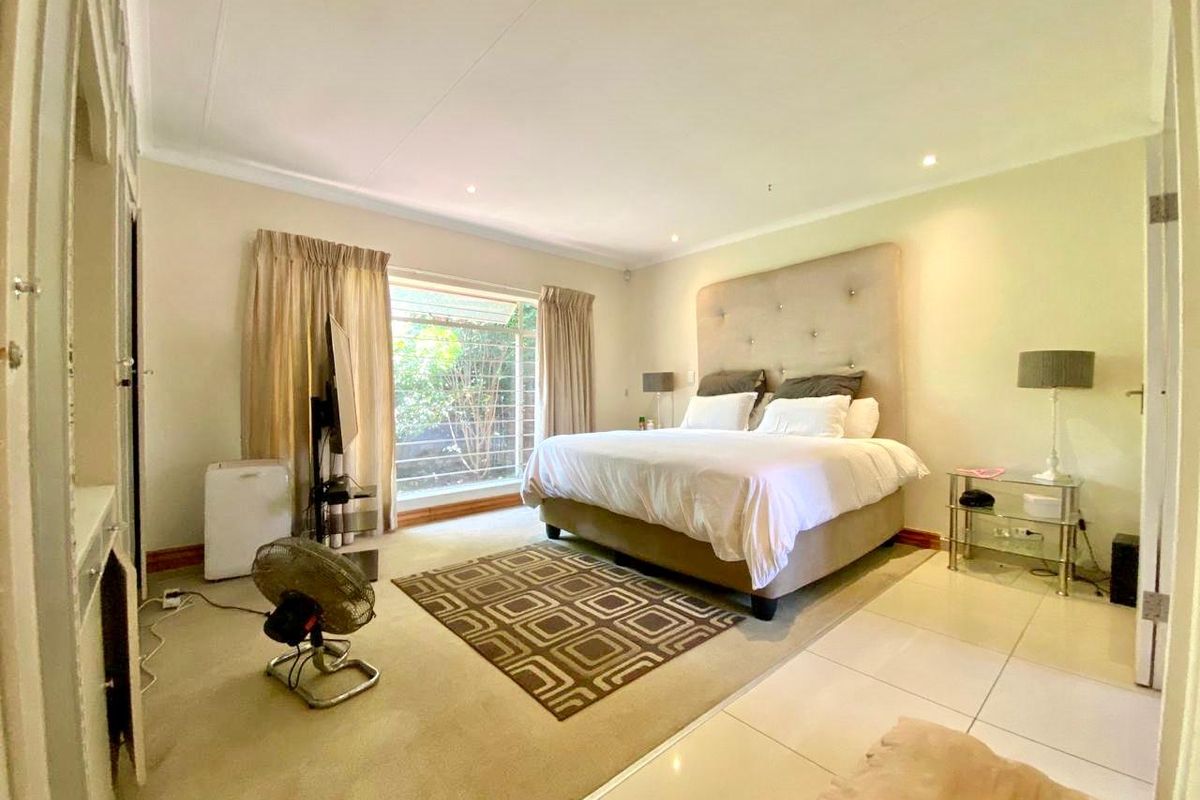 Spacious bedroom featuring large windows, built-in cupboards, and a mix of tiled and carpeted flooring.
