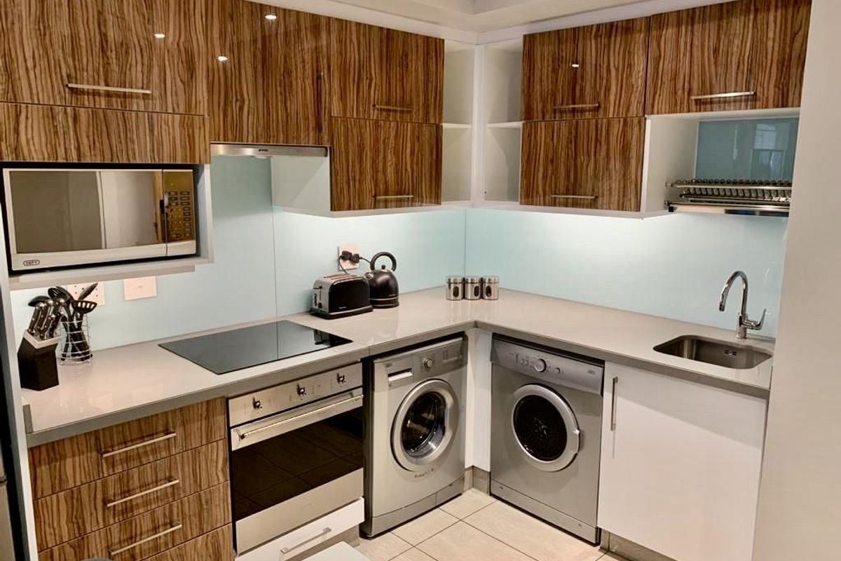 Modern kitchen featuring wood-grain cabinetry, stone countertops, glass splashback, integrated oven, hob, extractor fan, and built-in microwave.