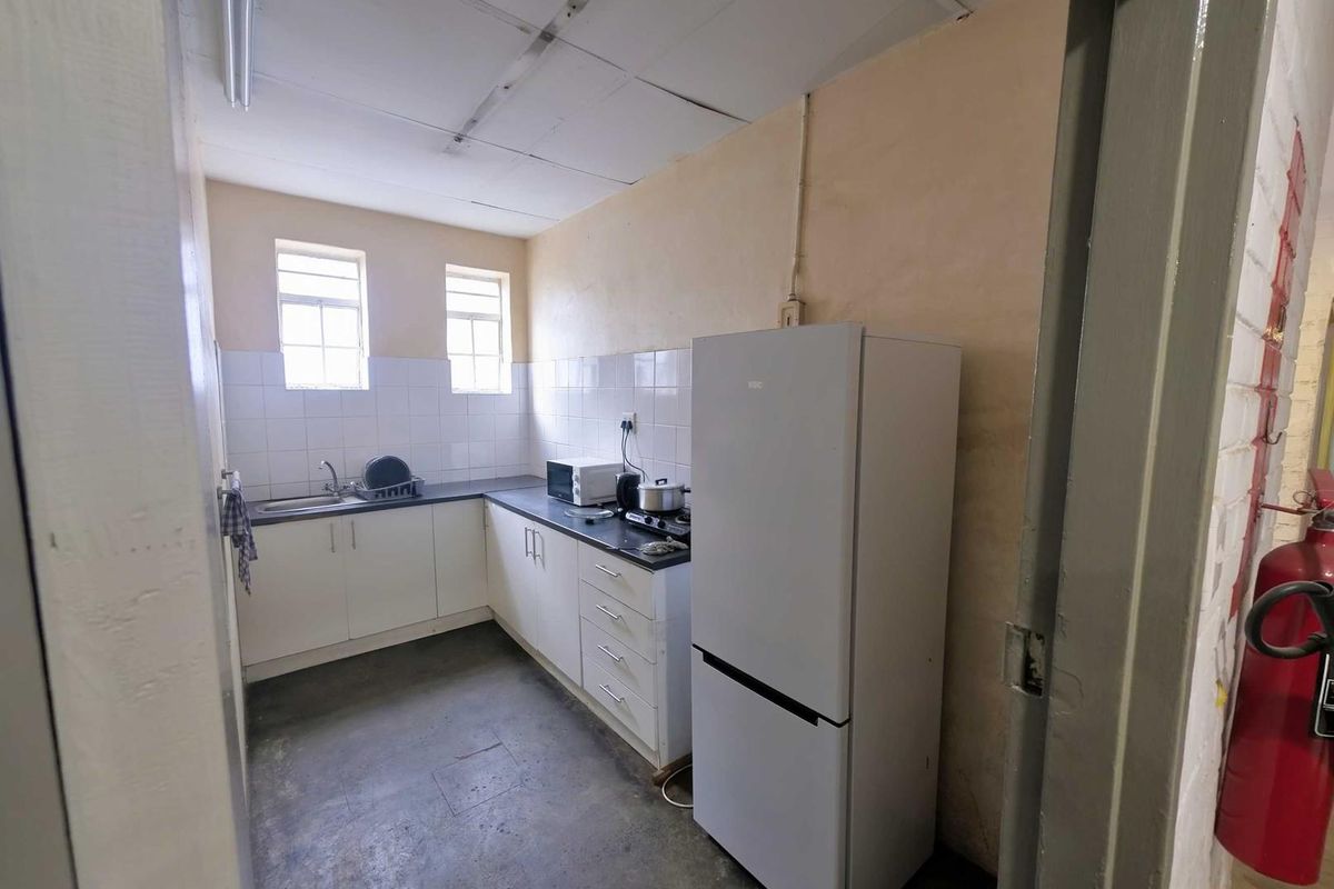 A functional industrial kitchenette featuring white cabinetry, a dark countertop, stainless steel sink, and tiled splashback, suitable for staff utility use.