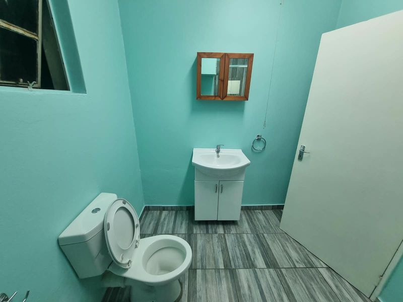 A functional bathroom featuring a vanity cabinet with basin, a toilet, and wall-mounted storage, finished with tiled flooring and bright wall paint.