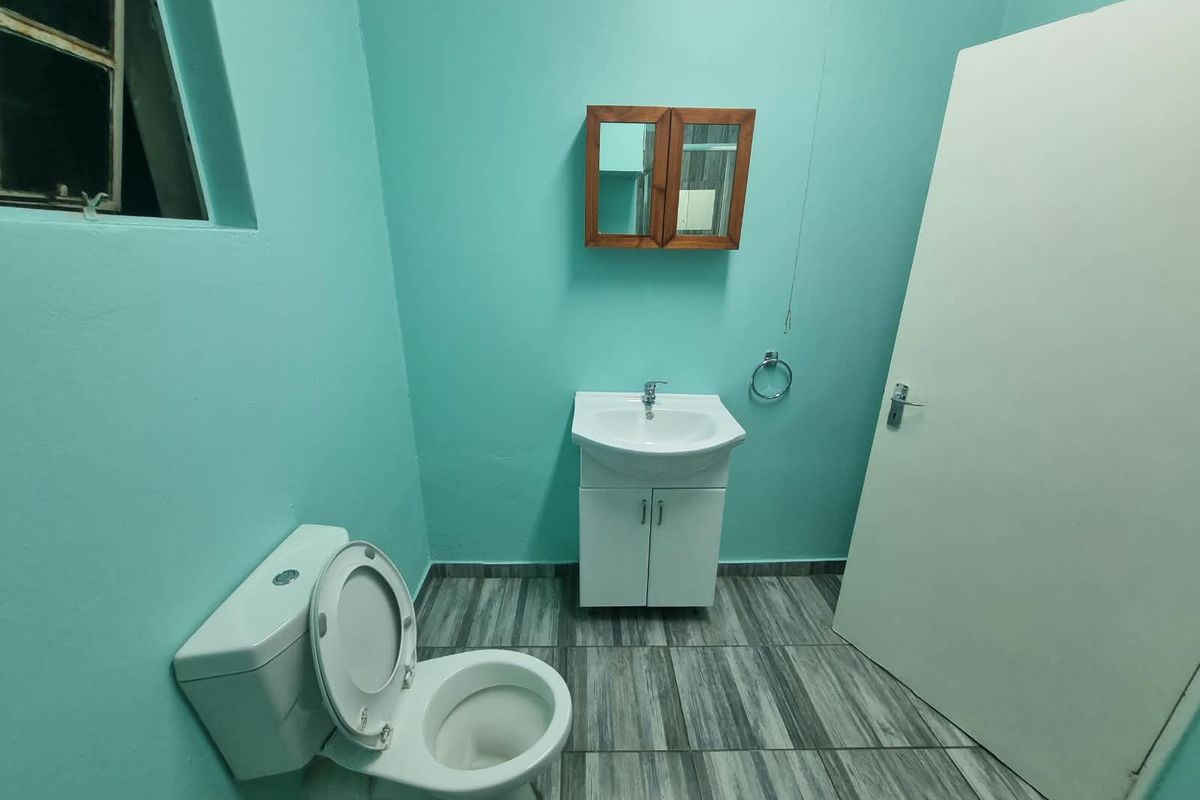A functional bathroom featuring a vanity cabinet with basin, a toilet, and wall-mounted storage, finished with tiled flooring and bright wall paint.