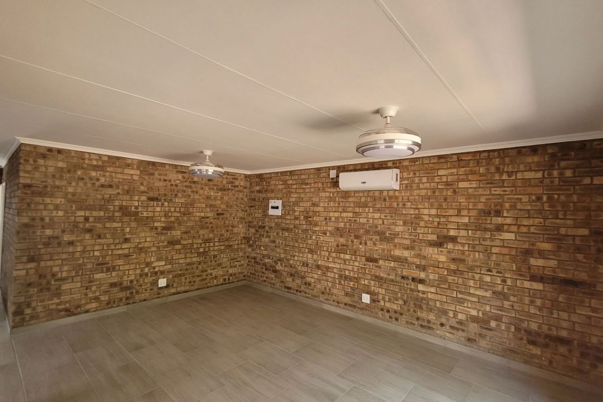 Spacious living area featuring exposed brick walls, tiled flooring, ceiling fans, and a wall-mounted air conditioning unit.
