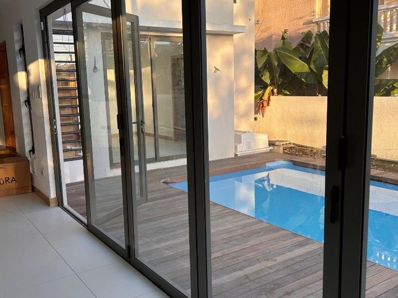 Modern indoor-outdoor transition featuring large bi-fold glass doors opening onto a timber deck and swimming pool area.