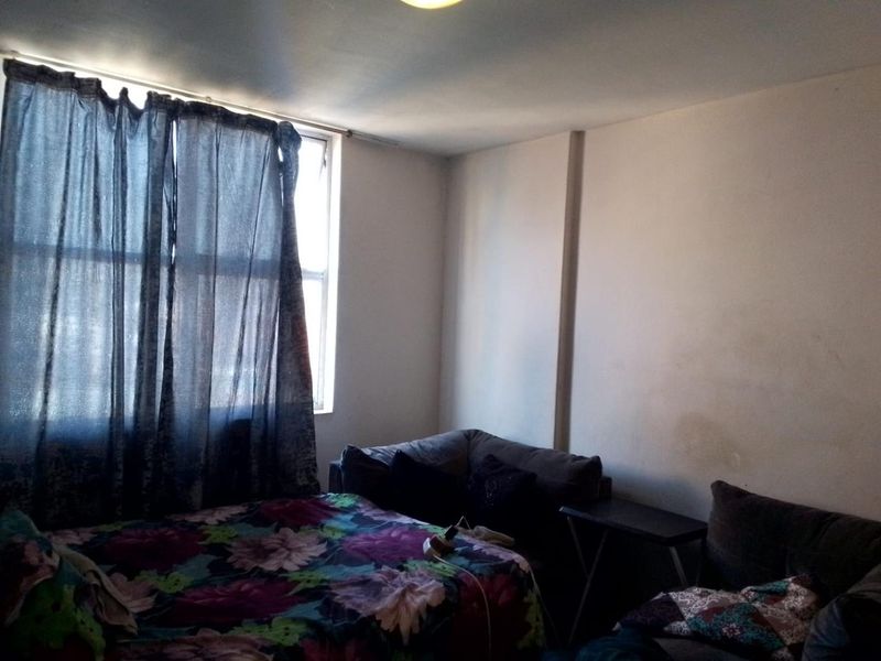 A bedroom featuring a window with a curtain rod, requiring cosmetic updates to the walls and general maintenance.
