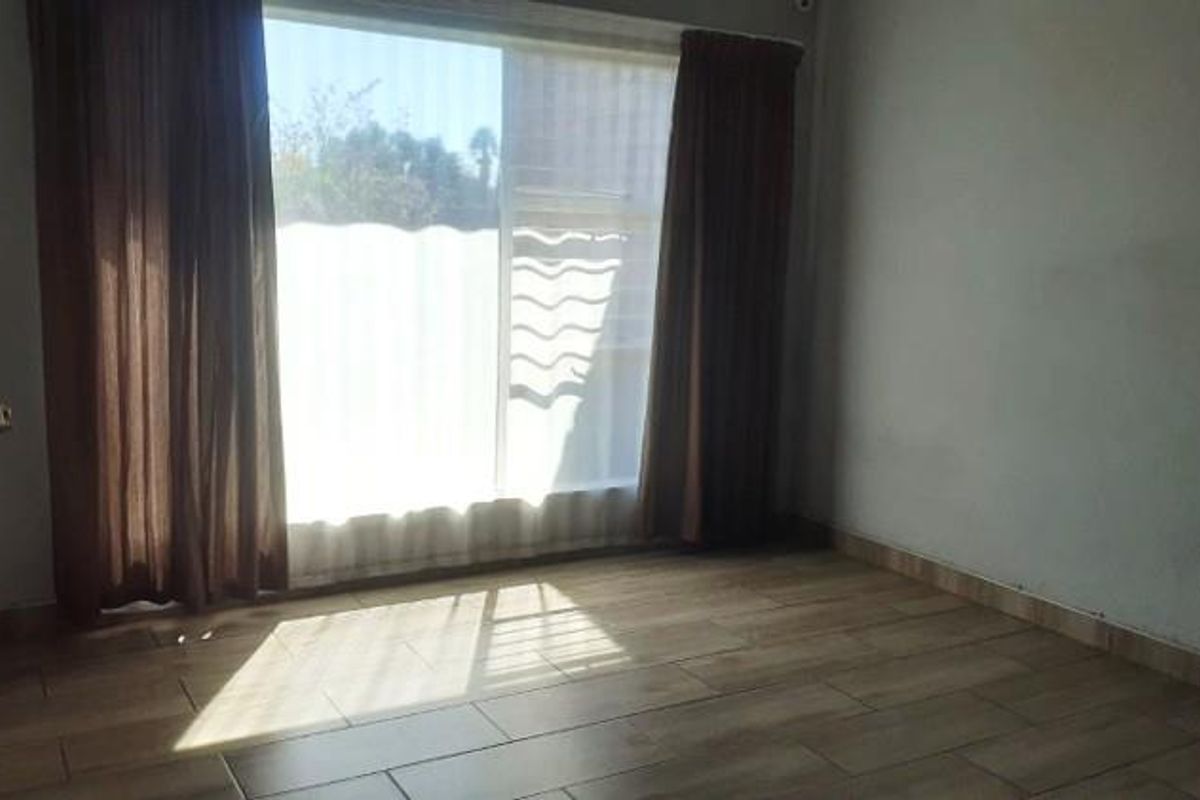 An empty bedroom featuring wood-look tile flooring and a large sliding glass door that provides natural light.