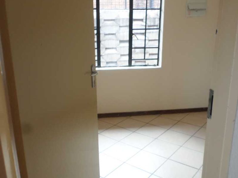An empty bedroom featuring tiled flooring and a window with security burglar bars.