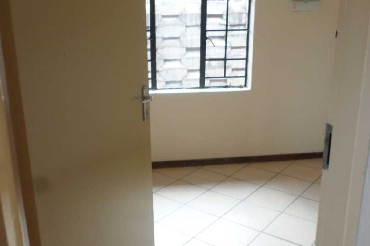 An empty bedroom featuring tiled flooring and a window with security burglar bars.