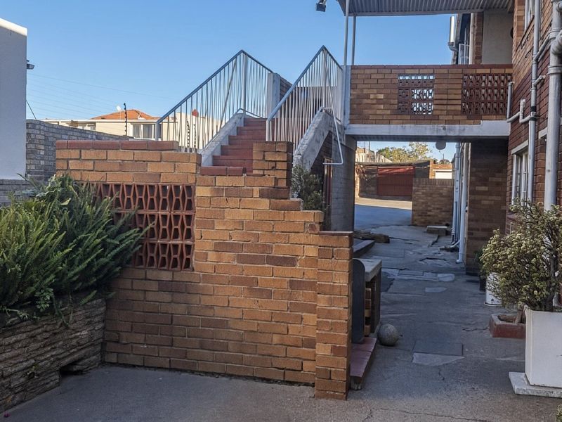 Rear exterior view of the townhouse featuring a brick staircase, metal railings, and paved walkway area with established brick boundary walls.