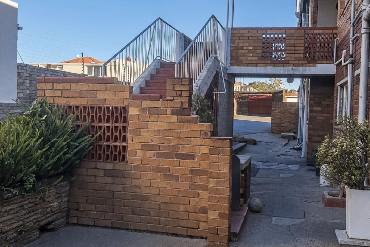 Rear exterior view of the townhouse featuring a brick staircase, metal railings, and paved walkway area with established brick boundary walls.