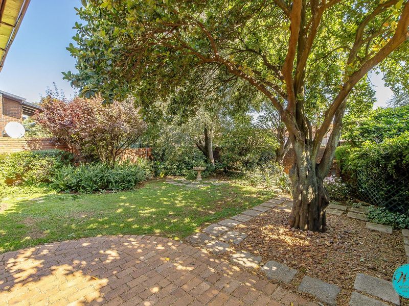 A private, well-established garden featuring mature trees, a brick-paved patio area, and brick boundary walls.