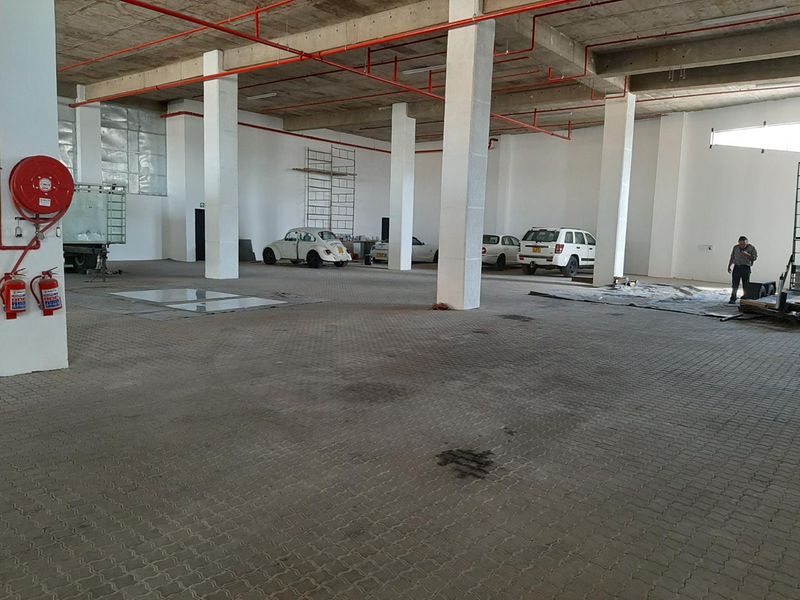Spacious industrial garage area featuring exposed fire suppression systems, concrete structural columns, and durable paved flooring, suitable for storage or workshop use.