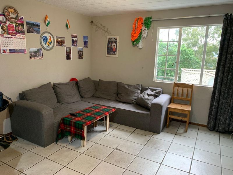 A living room area featuring tiled flooring and a window with security bars, offering a functional space with potential for cosmetic updates.
