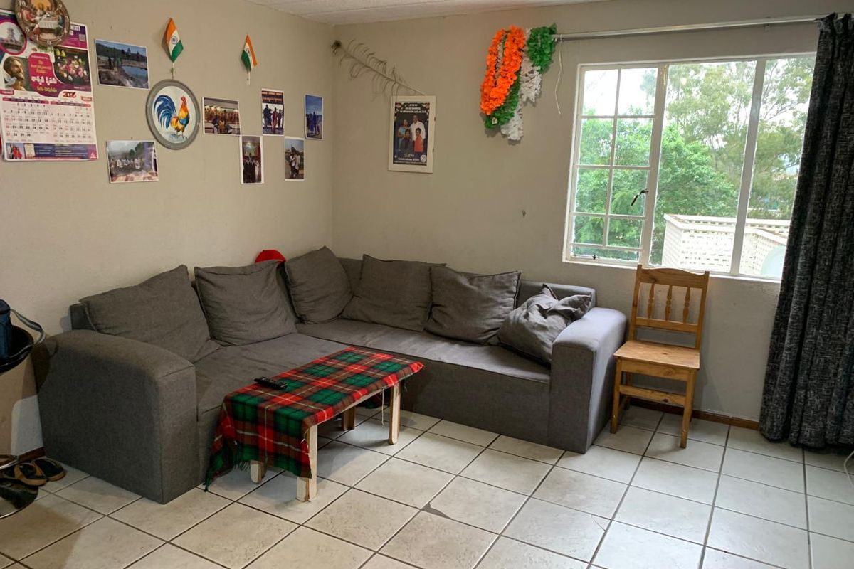 A living room area featuring tiled flooring and a window with security bars, offering a functional space with potential for cosmetic updates.