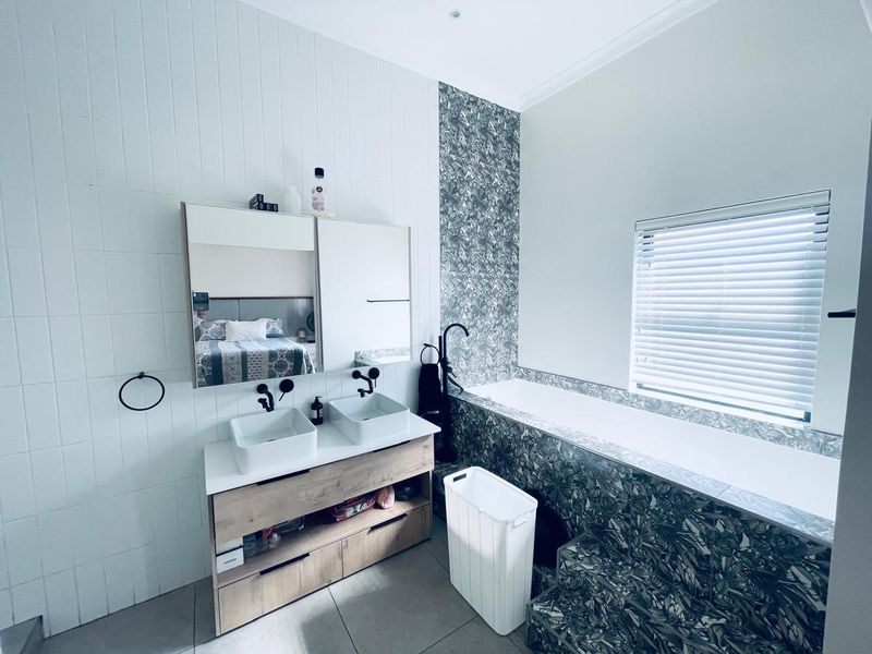 Modern bathroom featuring a double vanity with vessel sinks, matte black fixtures, and a tiled built-in bathtub with decorative patterned wall accents.