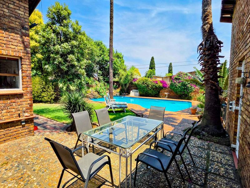 Outdoor entertainment area featuring a swimming pool, established garden, and brick-paved patio nestled between exposed brick building walls.