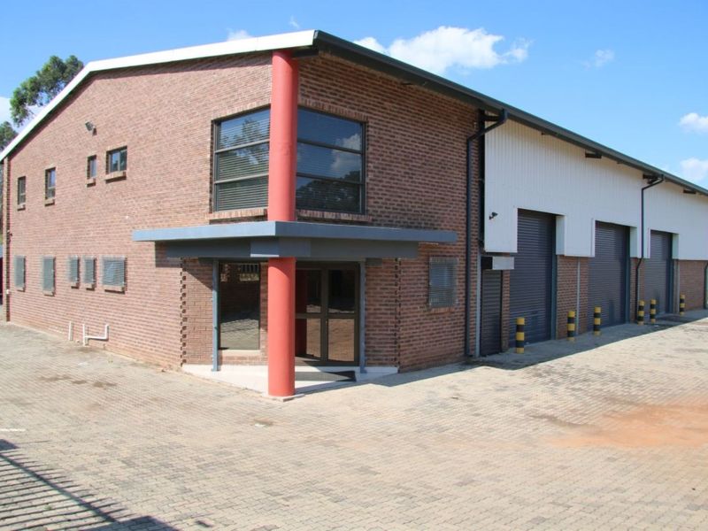 Industrial property featuring a brick facade, multiple roller shutter doors, and a paved driveway with security bollards.