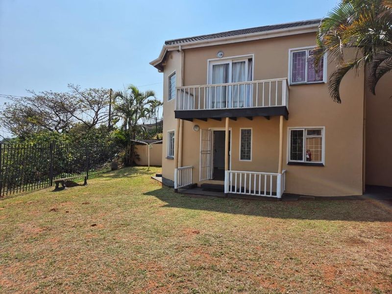Rear view of a two-story townhouse featuring a ground-floor patio, an upper-level balcony, and a private garden area with perimeter fencing.