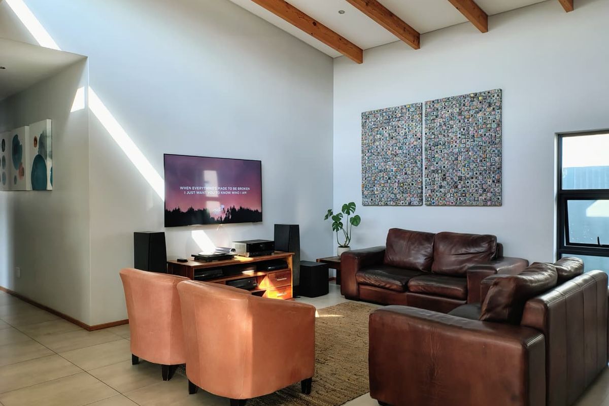 Spacious living room featuring high vaulted ceilings with exposed timber beams, large format floor tiles, and abundant natural light.
