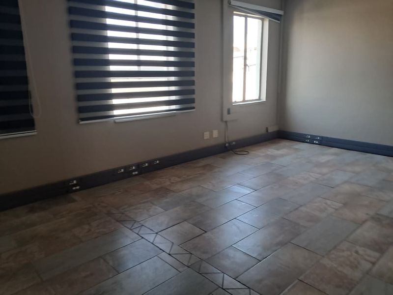 A spacious, empty office area featuring tiled flooring, modern zebra blinds, and integrated skirting board trunking for convenient electrical access.