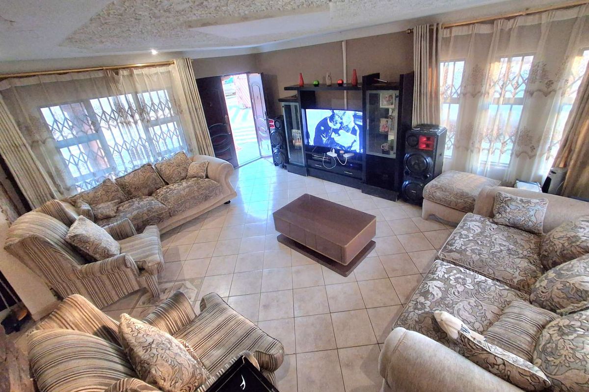 Spacious living room featuring tiled flooring, decorative ceiling detail, and large windows with security bars, providing a comfortable and functional family area.