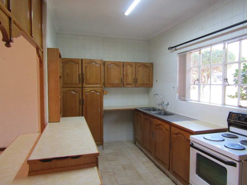 A functional kitchen featuring traditional wooden cabinetry, laminate countertops, a double stainless steel sink, and tiled splashbacks, offering potential for modern updates.