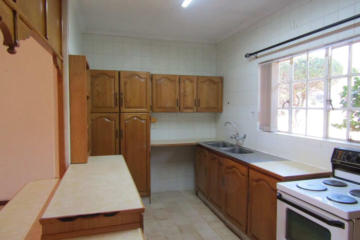 A functional kitchen featuring traditional wooden cabinetry, laminate countertops, a double stainless steel sink, and tiled splashbacks, offering potential for modern updates.