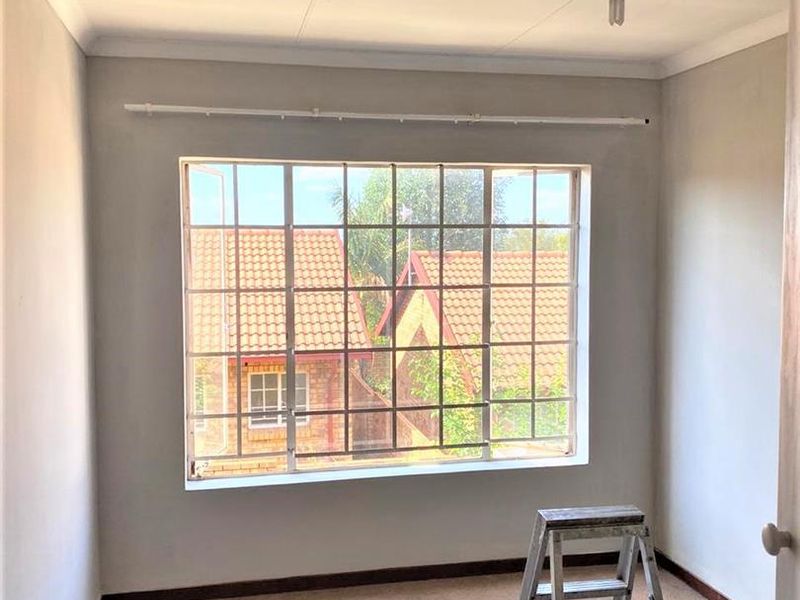 A vacant bedroom featuring a large window with security bars, neutral wall finishes, and carpeted flooring, ready for personalization.