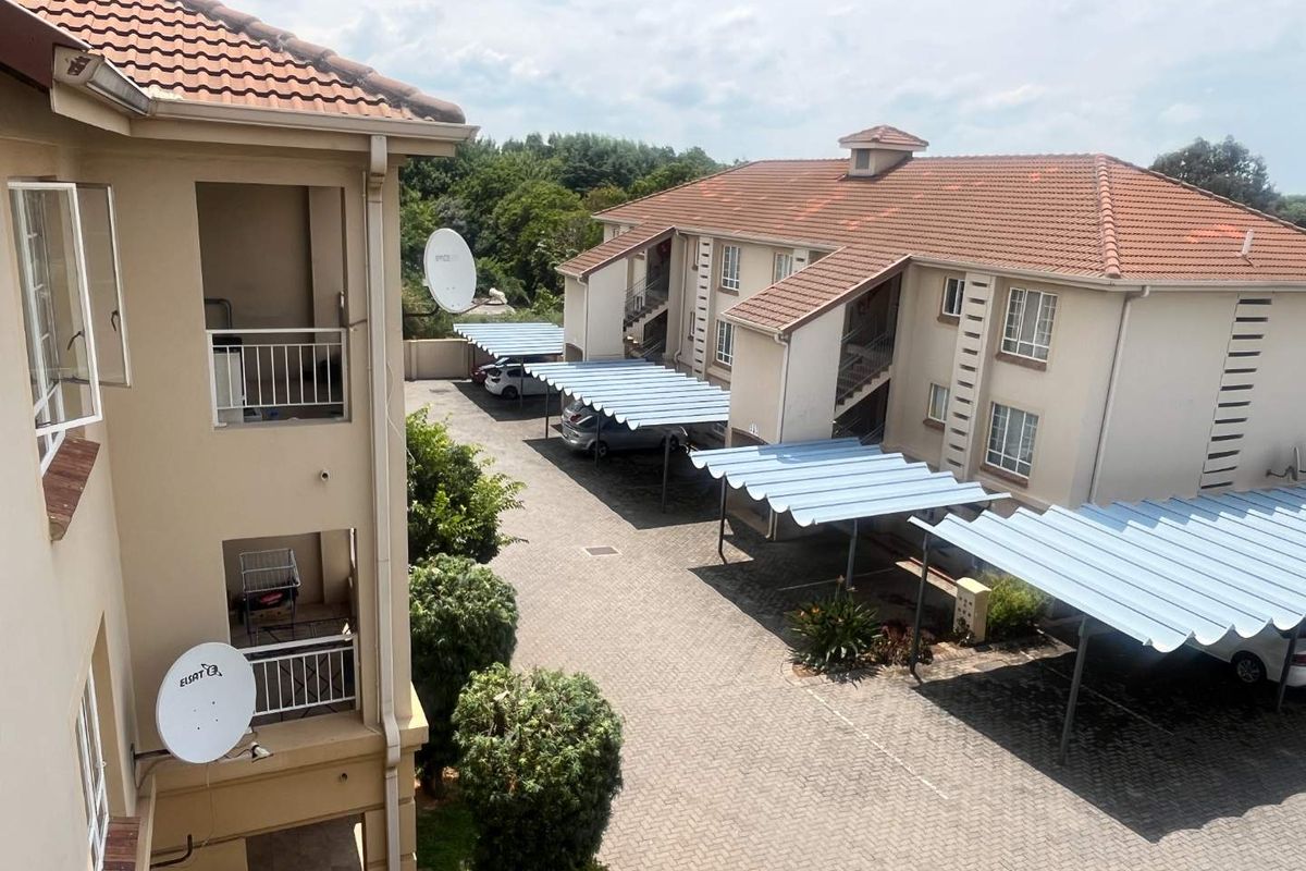 An elevated view of an apartment complex featuring paved parking areas with covered carports and multi-story residential buildings with tiled roofs.