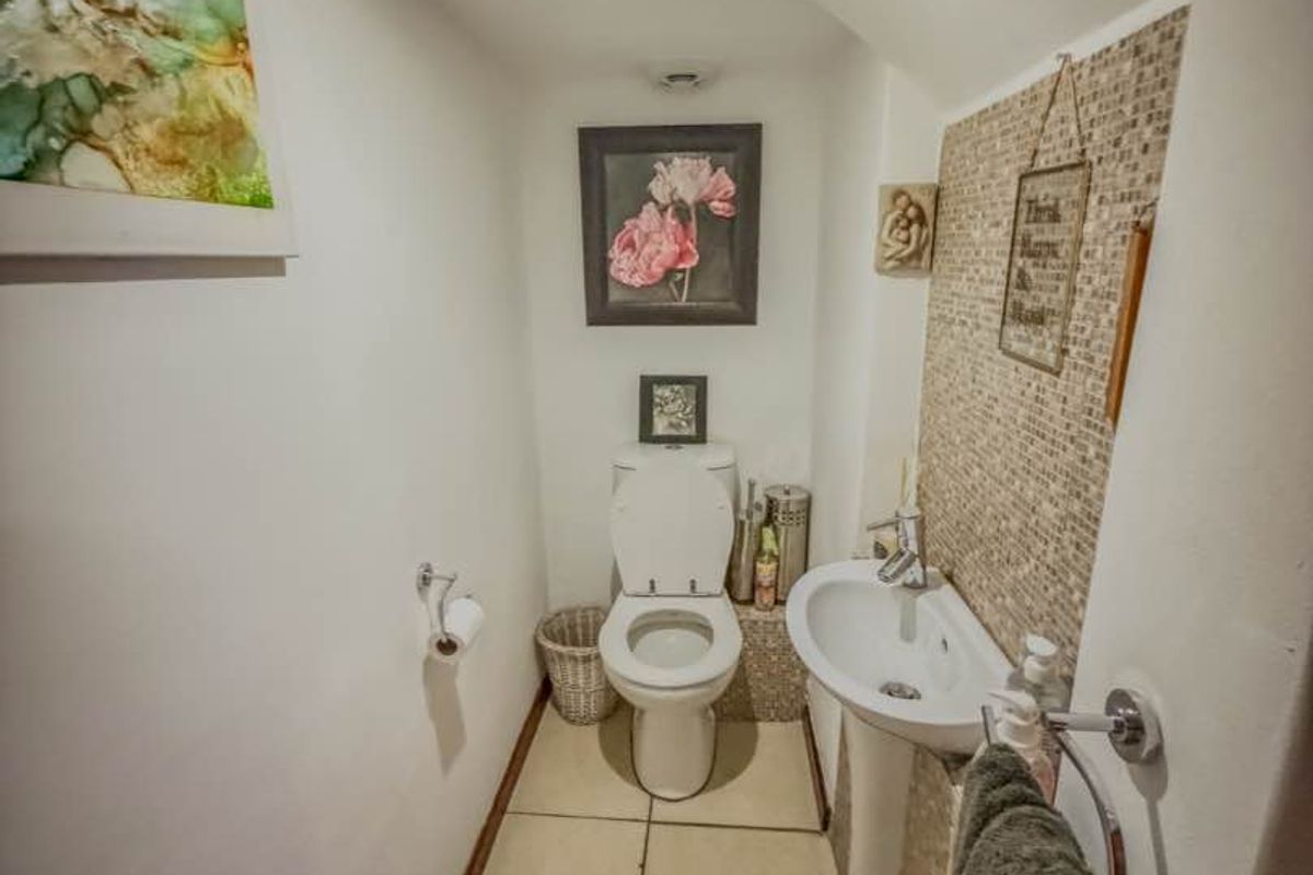 A compact guest bathroom featuring a pedestal sink, a toilet, and a decorative tiled feature wall.