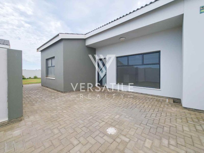 A modern exterior view of the property featuring a paved driveway, clean grey facade, and aluminium window frames.