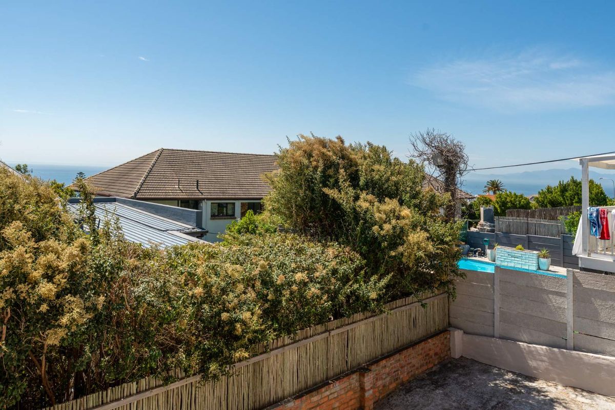 An elevated view of the rear garden area featuring a swimming pool, mature landscaping, and surrounding residential properties with distant coastal views.