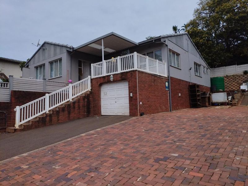 Front exterior view of a house featuring a brick base, raised balcony with white railing, garage, and a paved driveway.