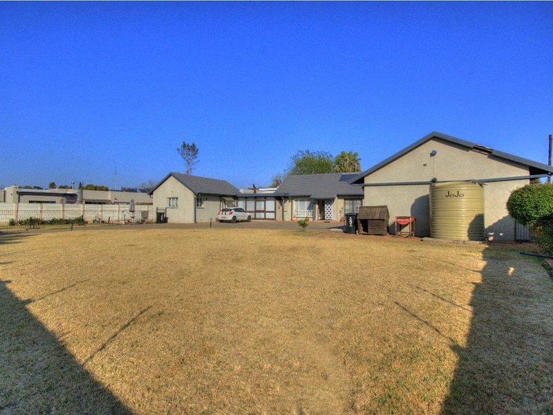 A spacious rear garden area featuring a large lawn, paved driveway, and a fixed water storage tank against the exterior wall of the house.