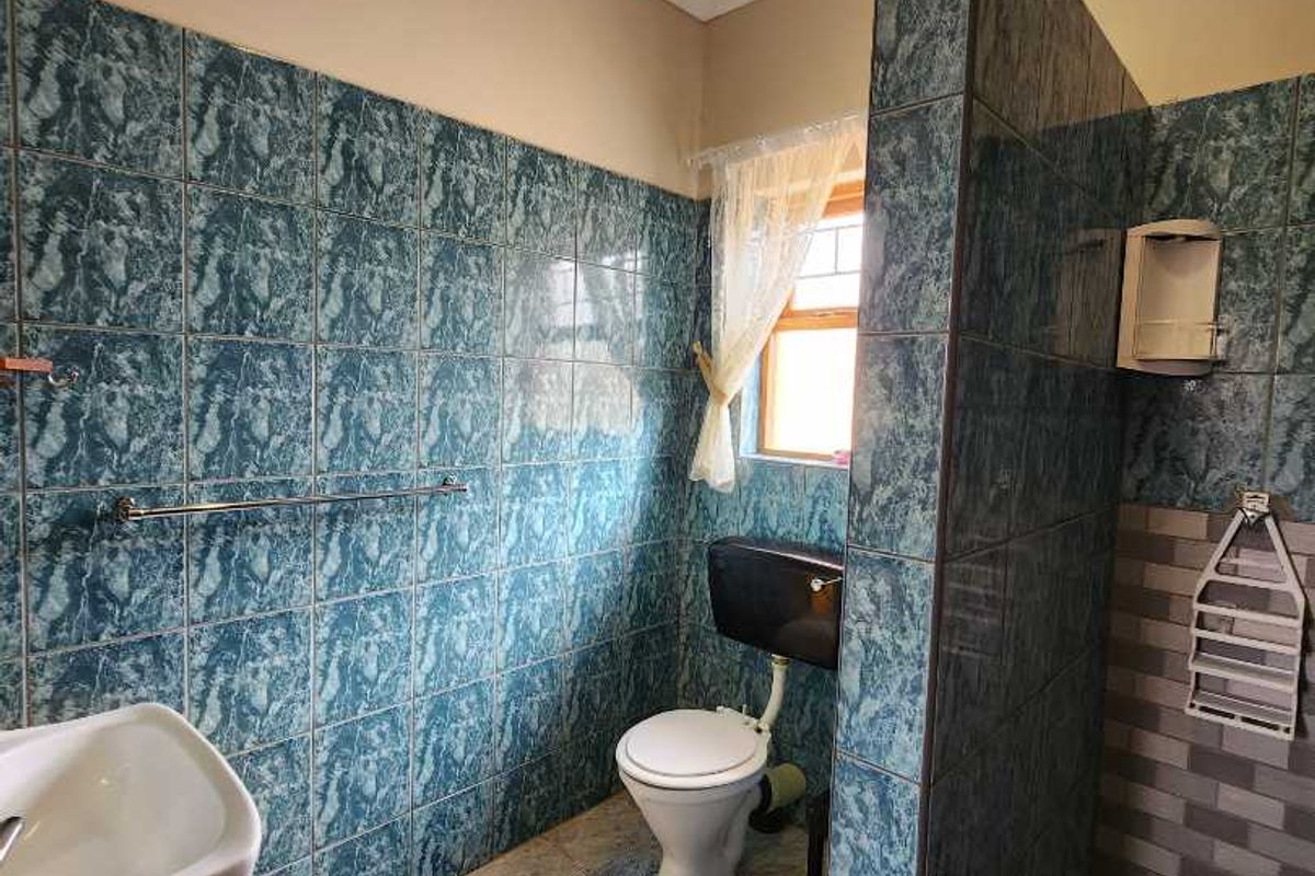 A functional bathroom featuring a walk-in shower enclosure, a standard toilet, and a wall-mounted basin with blue marble-effect wall tiling.