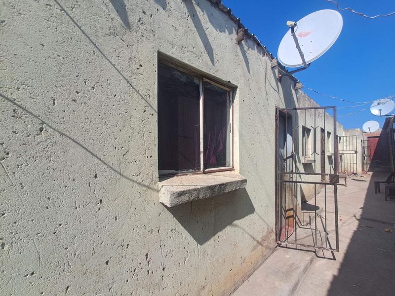 Exterior view of the property showing a weathered facade, security gate, and satellite dish installation.