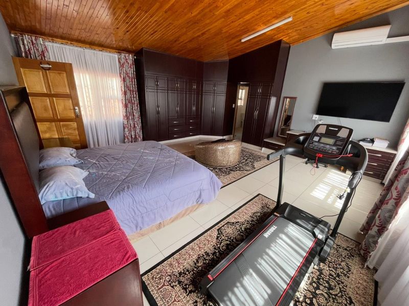 Spacious bedroom featuring extensive built-in cabinetry, a warm timber ceiling, tiled flooring, and an integrated air conditioning unit.