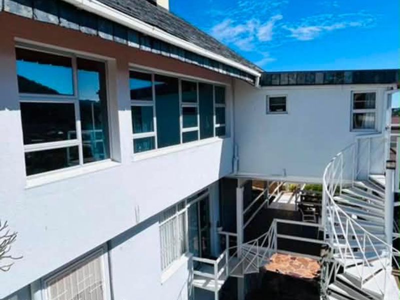Rear exterior view of the property featuring a white spiral staircase, stone paved patio area, and large windows.
