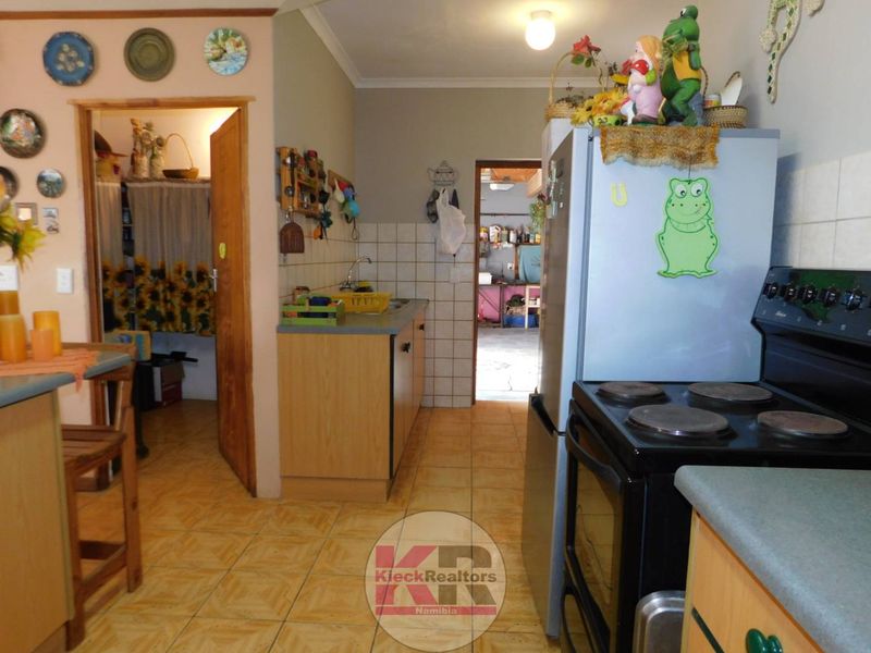 A functional kitchen featuring tiled flooring, a tiled backsplash, built-in cabinetry, and a freestanding stove, with direct access to adjacent rooms.