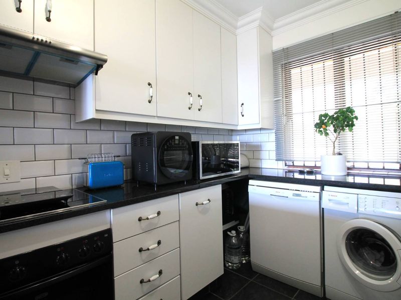 Modern kitchen featuring white cabinetry, black granite countertops, subway tile backsplash, and integrated appliances including a dishwasher and washing machine.