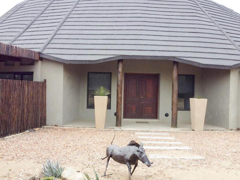 Front elevation of a house featuring a distinctive thatched roof, timber support columns, and a double timber entrance door with a gravel driveway.