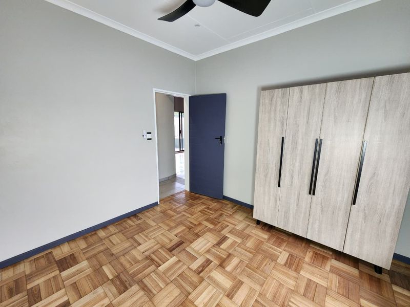 A bright, empty bedroom featuring well-maintained parquet flooring, a ceiling fan, and neutral wall finishes.