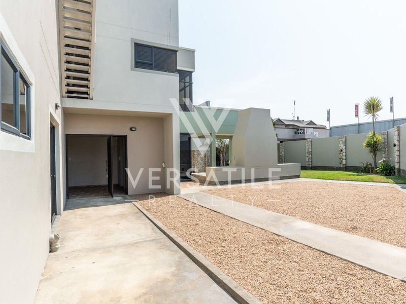 Rear exterior view featuring a concrete patio, built-in braai area, gravel landscaping, and a secure boundary wall.