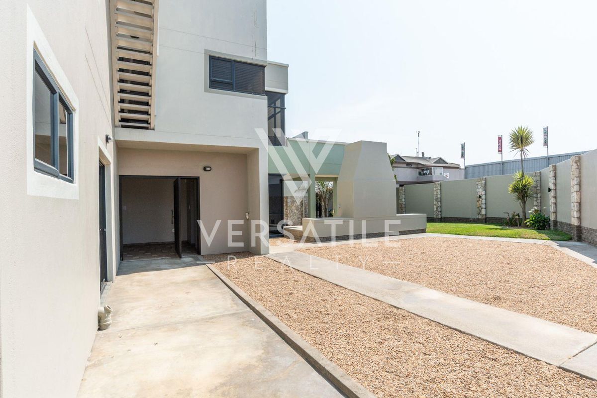 Rear exterior view featuring a concrete patio, built-in braai area, gravel landscaping, and a secure boundary wall.
