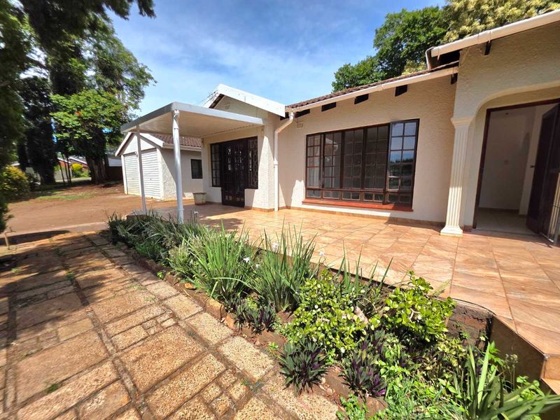 A well-maintained rear exterior featuring a spacious tiled patio, covered outdoor area, and established garden beds with paved pathways.