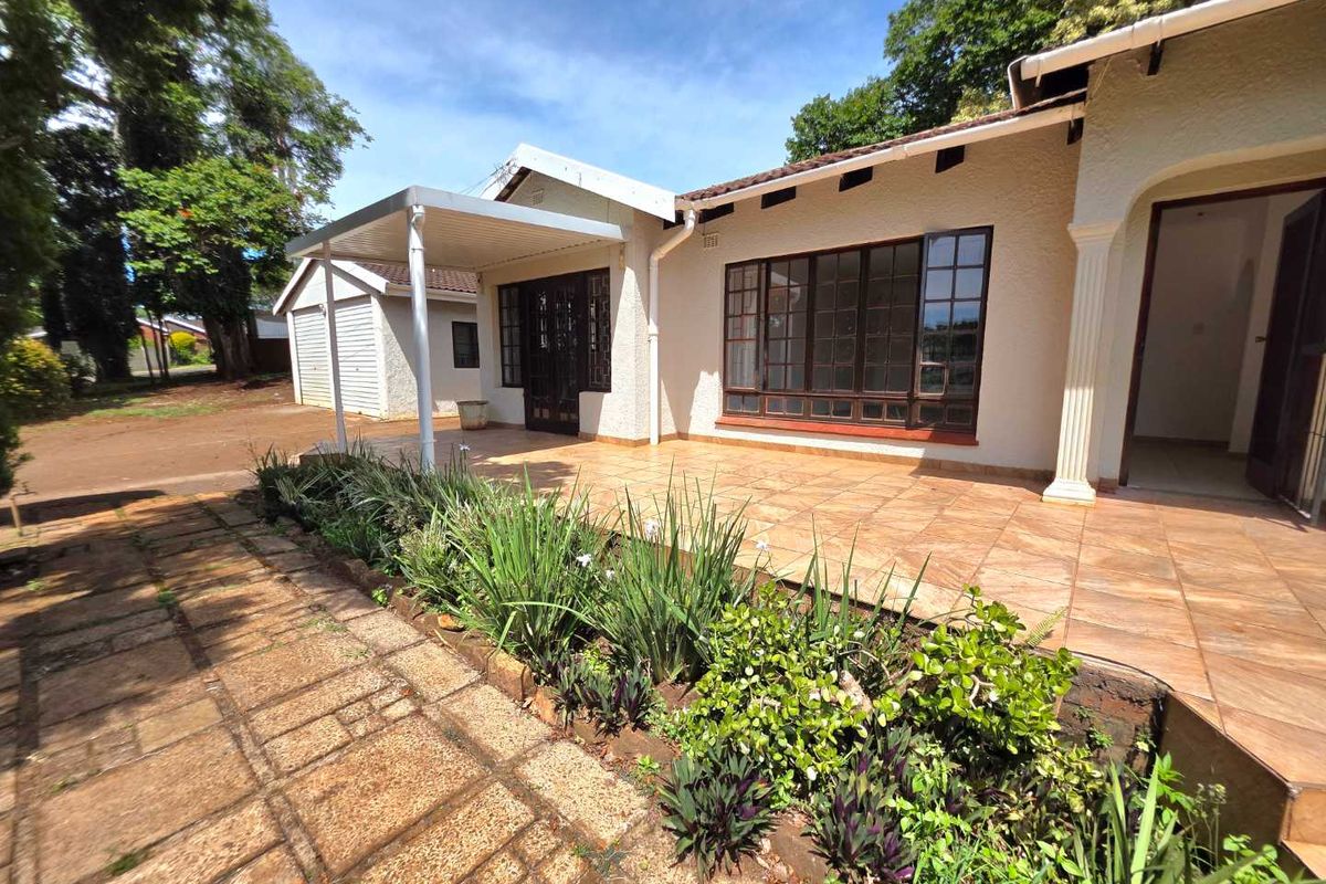 A well-maintained rear exterior featuring a spacious tiled patio, covered outdoor area, and established garden beds with paved pathways.